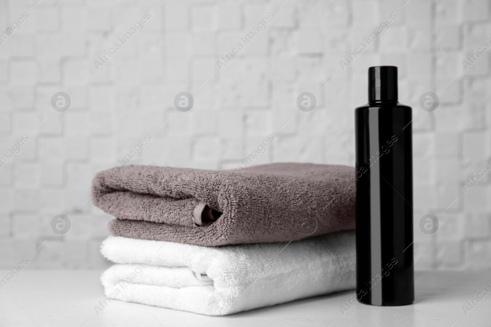 Photo of Folded towels and shampoo on table against white wall