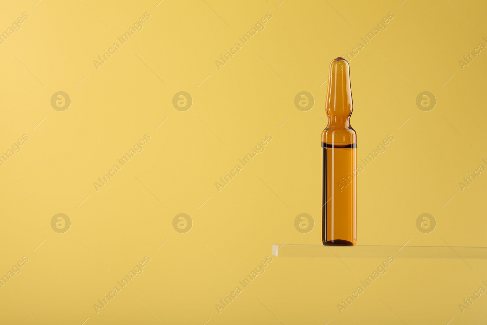 Photo of Glass ampoule with liquid on yellow background. Space for text