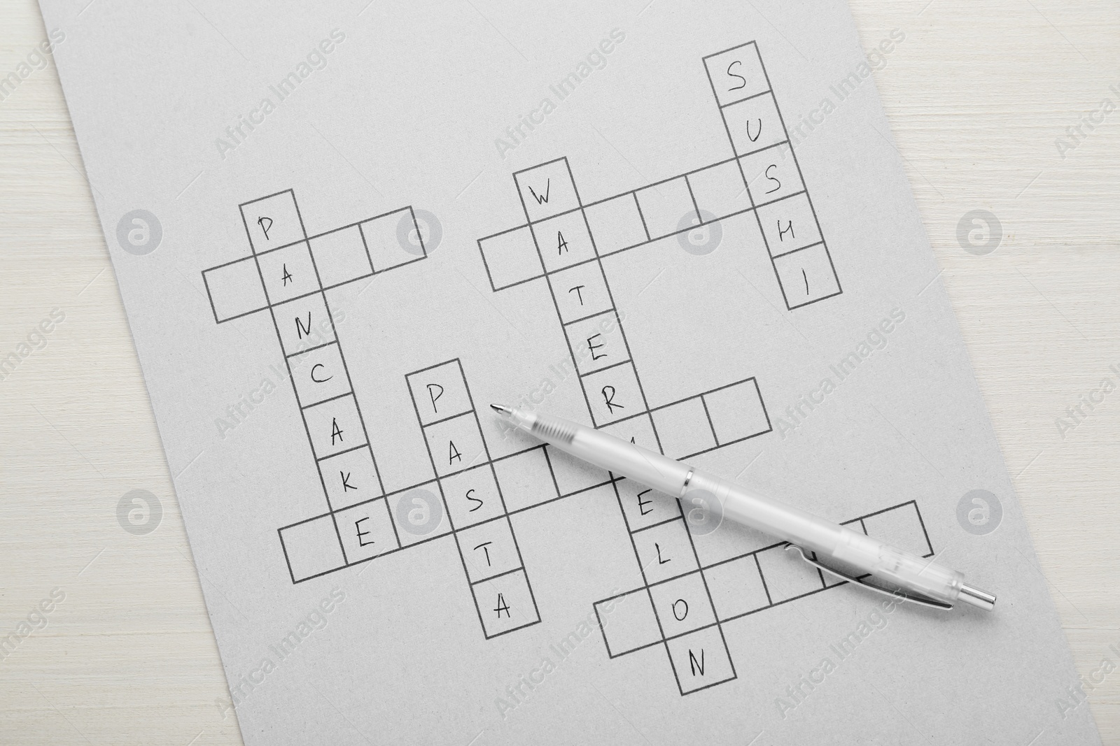 Photo of Crossword with answers and pen on white wooden table, top view