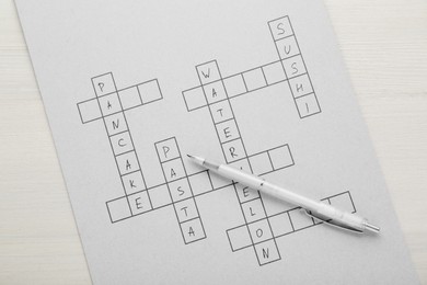 Crossword with answers and pen on white wooden table, top view