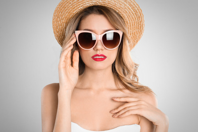 Young woman wearing stylish sunglasses and hat on light grey background