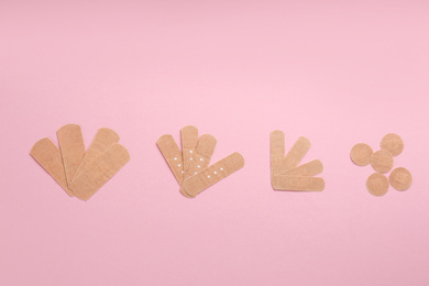 Different types of sticking plasters on pink background, flat lay