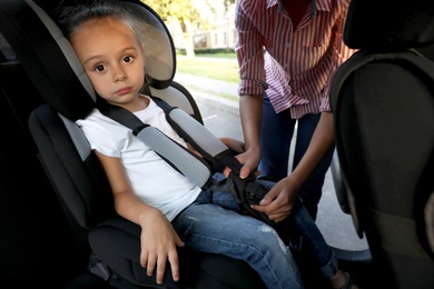 Mother fastening her daughter with car safety seat belt. Family vacation