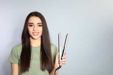 Happy woman with hair iron on grey background. Space for text