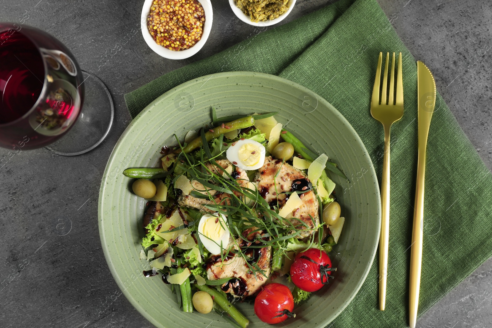 Photo of Delicious dish with tarragon, salad dressings and glass of wine served on grey table, flat lay