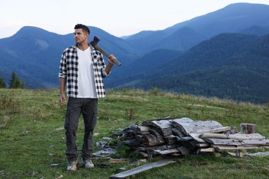 Photo of Handsome man with axe and cut firewood in mountains