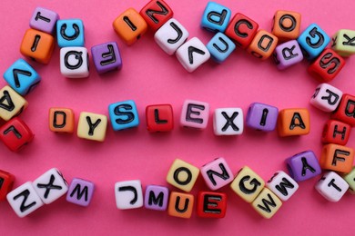 Colorful beads with word Dyslexia on pink background, flat lay