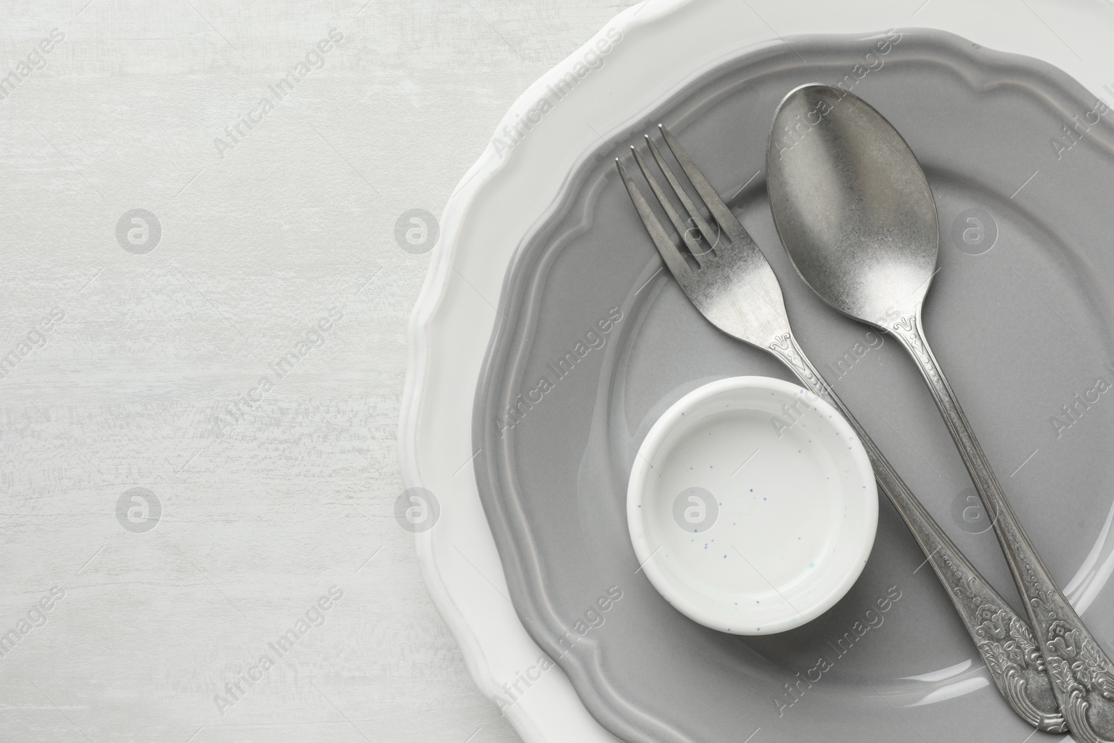 Photo of Stylish setting with cutlery, bowl and plates on light textured table, top view. Space for text