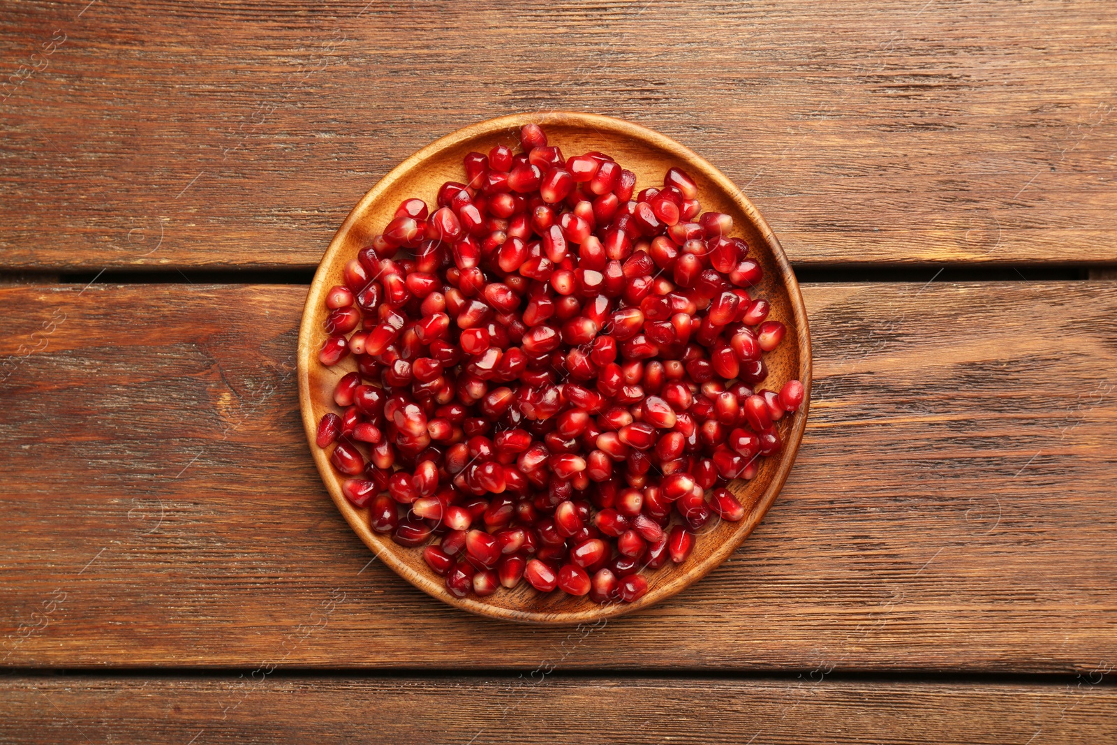 Photo of Tasty ripe pomegranate grains on wooden table, top view