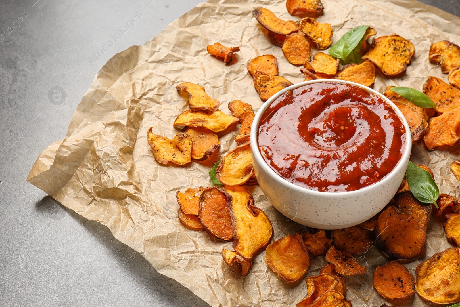 Photo of Sweet potato chips and bowl of sauce served on grey table