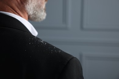 Bearded man with dandruff on his jacket against grey background, closeup. Space for text