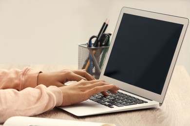 African-American woman typing on laptop at wooden table indoors, closeup