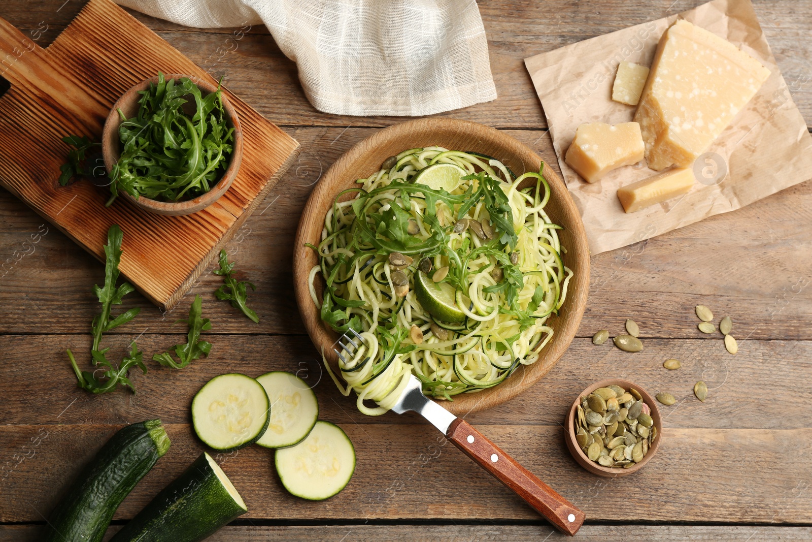 Photo of Delicious zucchini pasta with pumpkin seeds, lime and arugula served on wooden table, flat lay
