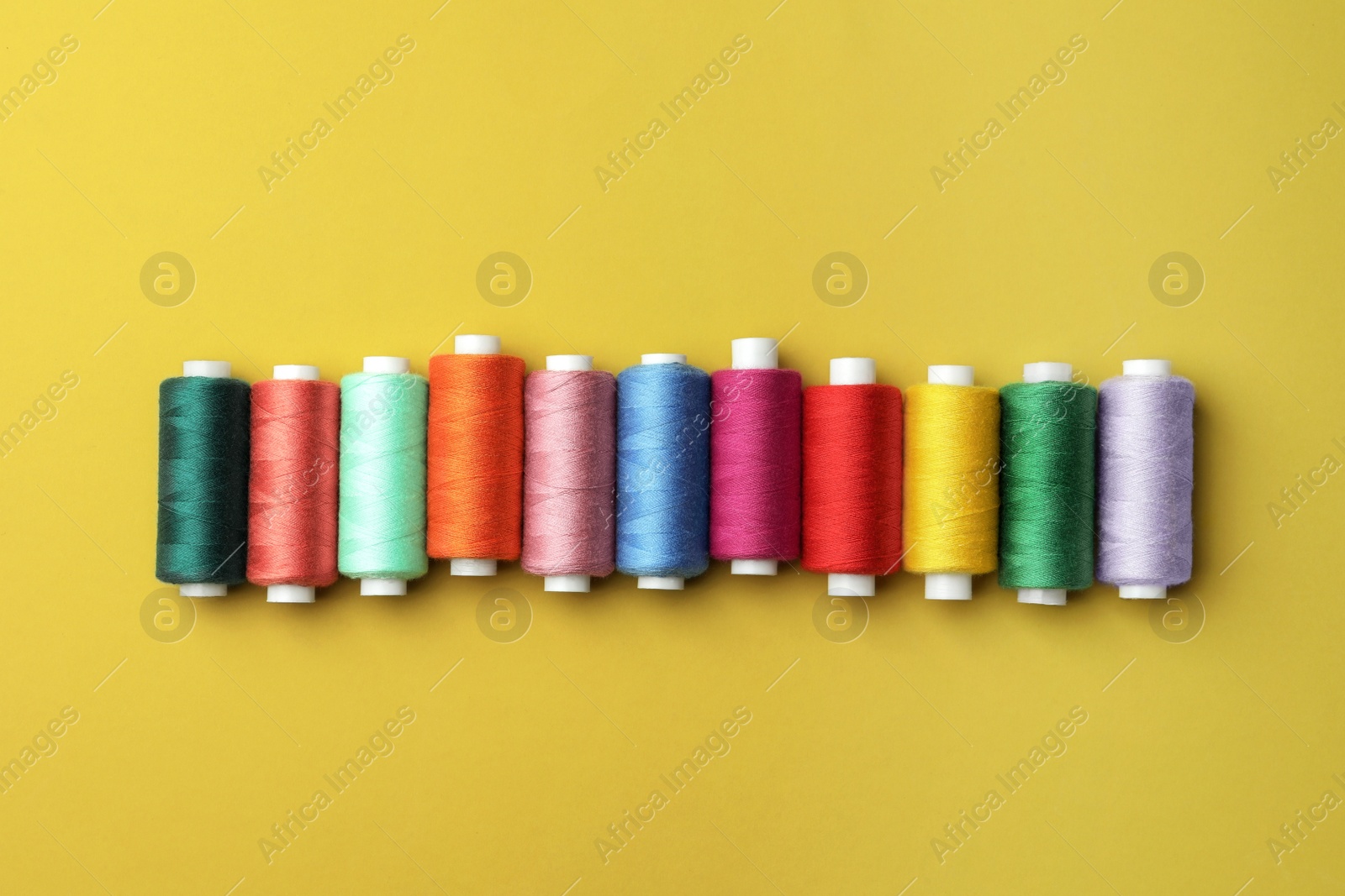 Photo of Set of colorful sewing threads on yellow background, flat lay