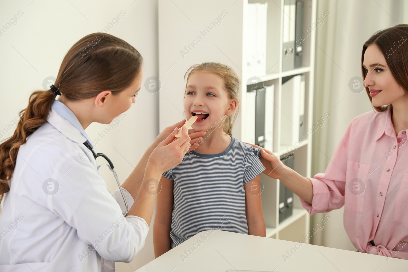 Photo of Mother and daughter visiting pediatrician. Doctor examining little patient's throat in hospital