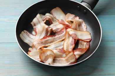 Delicious bacon slices in frying pan on light blue wooden table