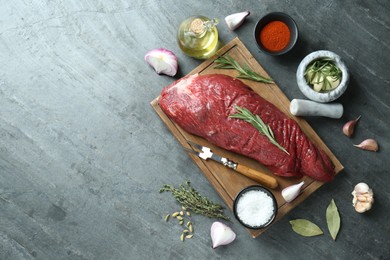 Photo of Piece of raw beef meat and spices on grey table, flat lay. Space for text