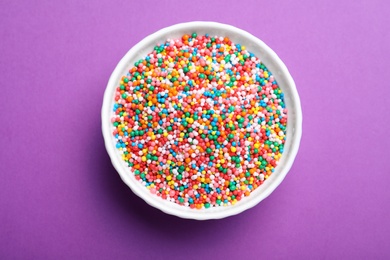 Photo of Colorful sprinkles in bowl on purple background, top view. Confectionery decor