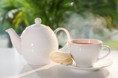 Teapot and cup of delicious morning drink with meringue on white table
