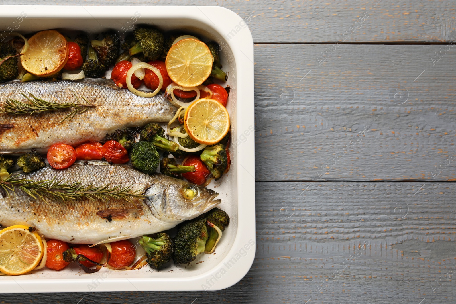 Photo of Delicious fish with vegetables and lemon in baking dish on grey wooden table, top view. Space for text