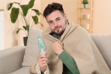 Photo of Sick man holding nebulizer for inhalation on sofa at home