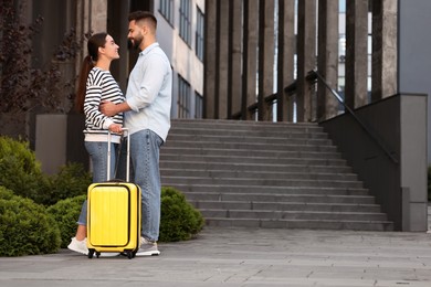Photo of Long-distance relationship. Beautiful young couple with suitcase near building outdoors