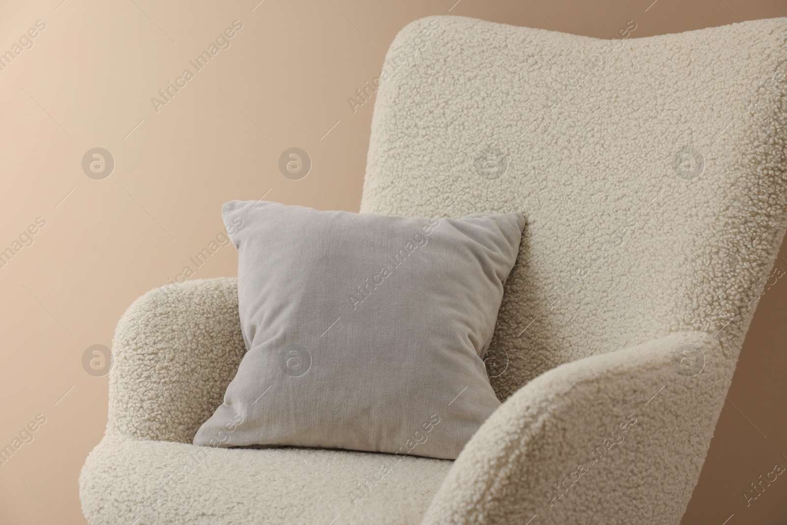 Photo of Soft grey pillow on armchair near beige wall