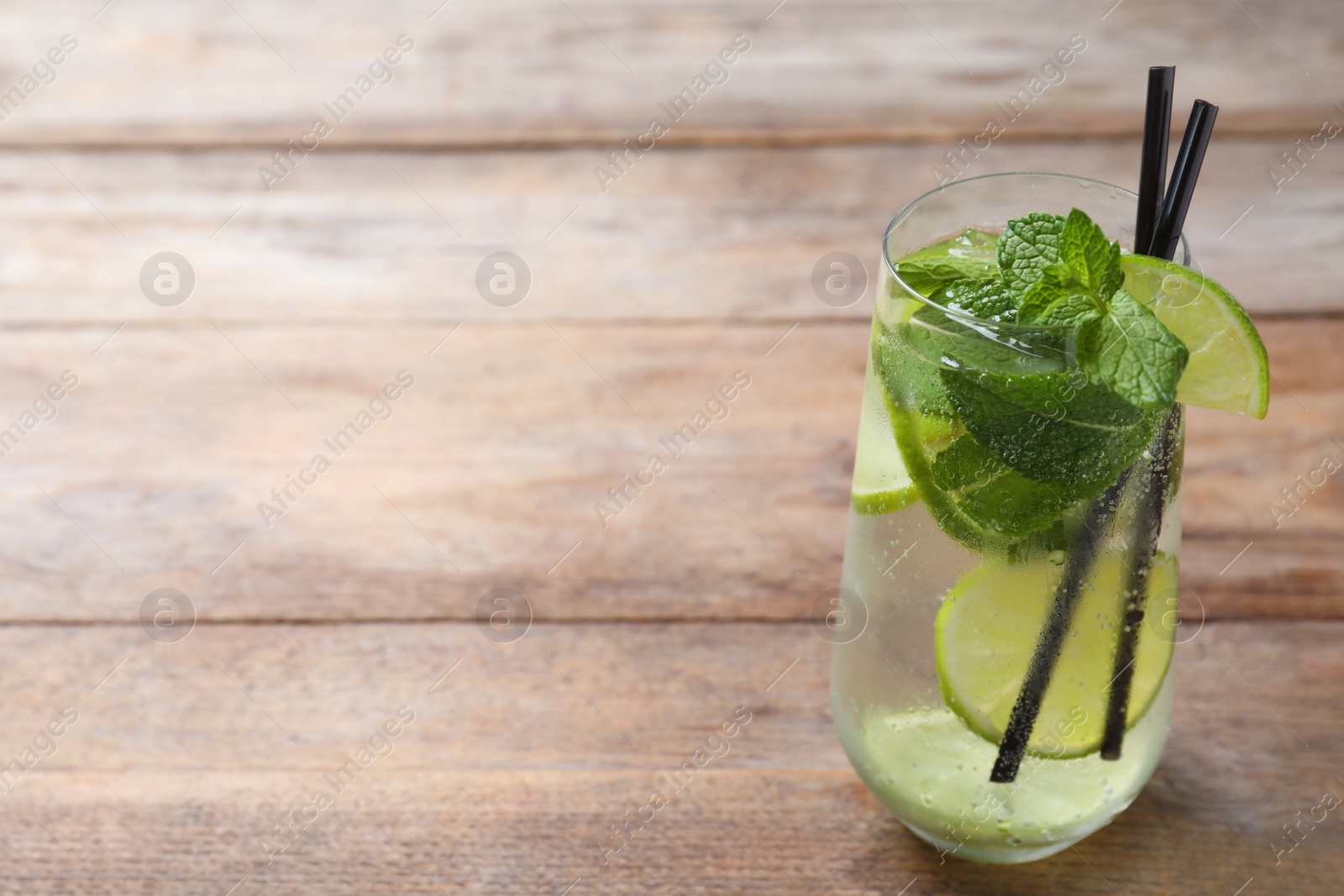 Photo of Glass of tasty refreshing cocktail with lime and mint on wooden table. Space for text