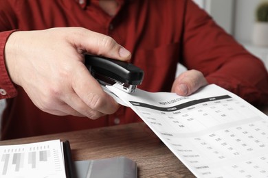 Man with documents using stapler at wooden table, closeup