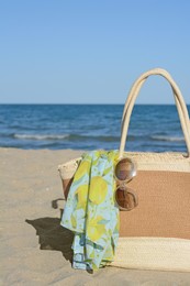 Photo of Straw bag with beach wrap and sunglasses on sandy seashore. Summer accessories