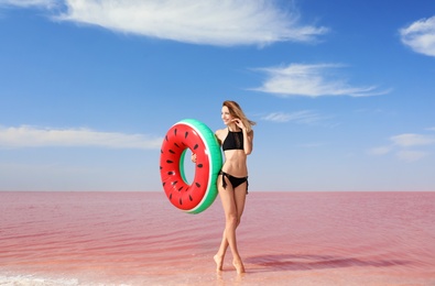 Beautiful woman with inflatable ring posing near pink lake on sunny day