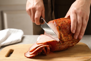 Woman cutting ham on wooden board at table, closeup