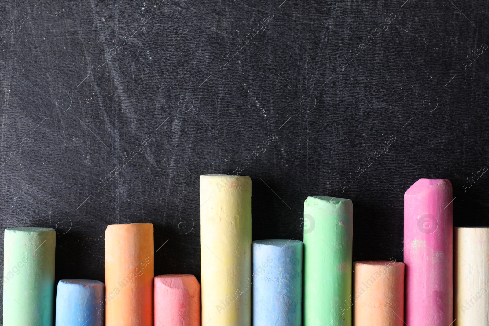 Photo of Pieces of color chalk on blackboard, flat lay. Space for text