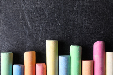 Photo of Pieces of color chalk on blackboard, flat lay. Space for text