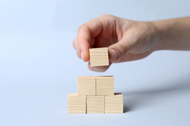 Photo of Woman building pyramid of cubes on light background, closeup with space for text. Idea concept