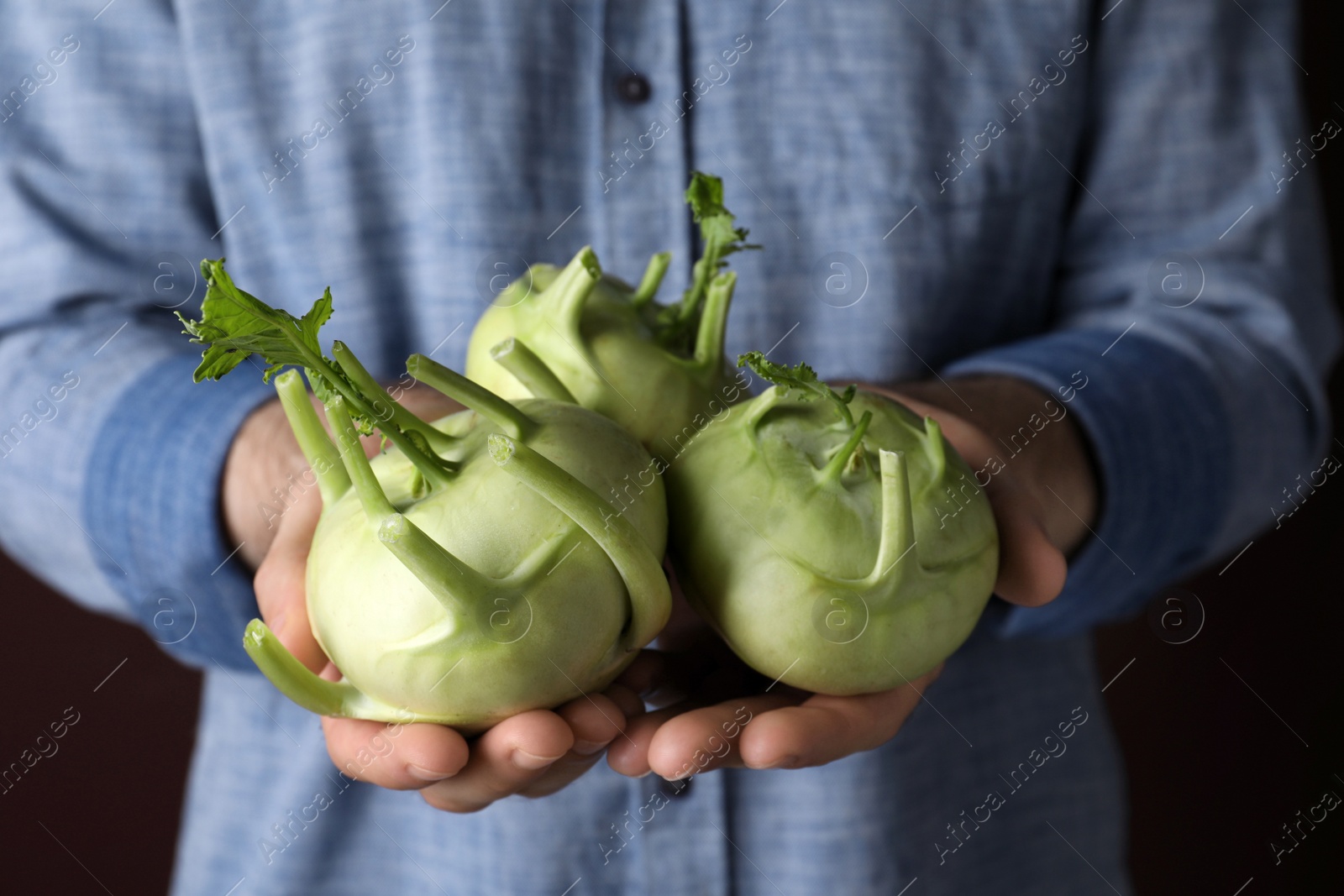 Photo of Man with ripe kohlrabi plants on brown background, closeup