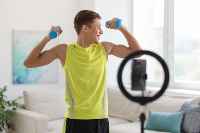 Smiling sports blogger working out with dumbbells while streaming online fitness lesson at home