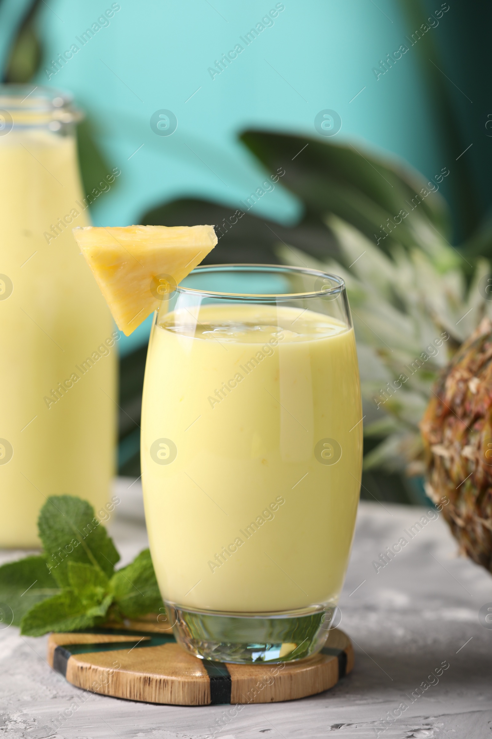 Photo of Tasty pineapple smoothie, mint and fruit on grey textured table