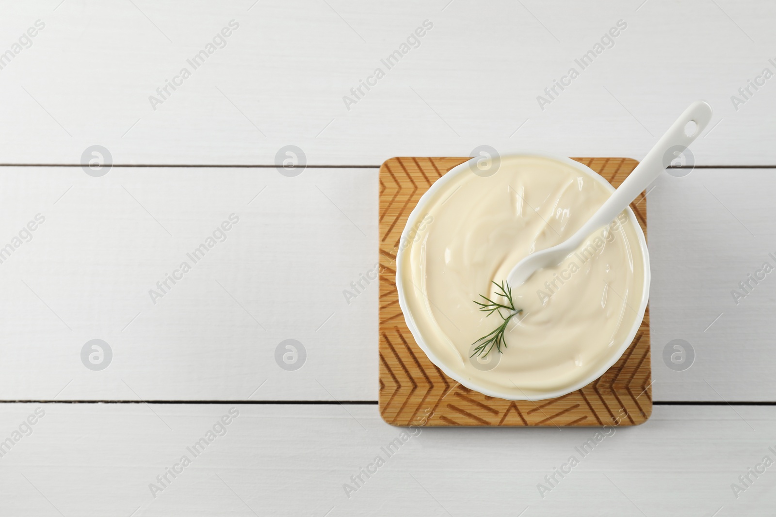 Photo of Fresh mayonnaise sauce in bowl on white wooden table, top view. Space for text