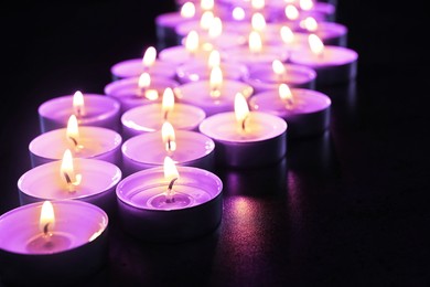 Image of Beautiful burning violet candles on black background. Funeral attributes