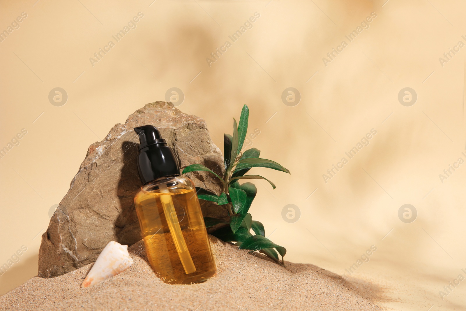 Photo of Bottle of serum, stone and green leaves on sand against beige background. Space for text