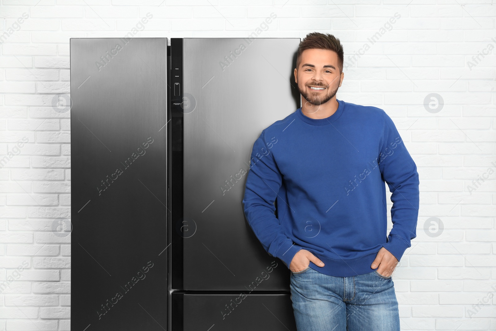 Photo of Happy young man near modern refrigerator indoors