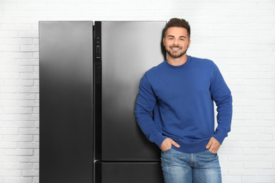 Photo of Happy young man near modern refrigerator indoors