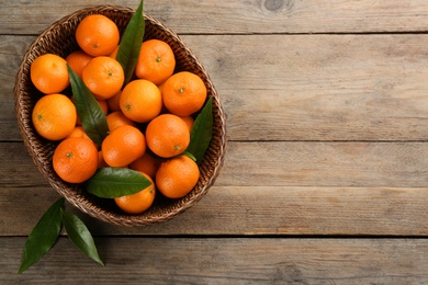 Photo of Fresh ripe tangerines with green leaves on wooden table, top view. Space for text