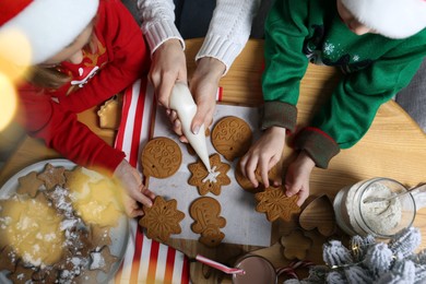 Photo of Mother and her little children decorating tasty Christmas cookies at wooden table, top view