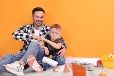 Photo of Father and son with repair tools near orange wall, space for text