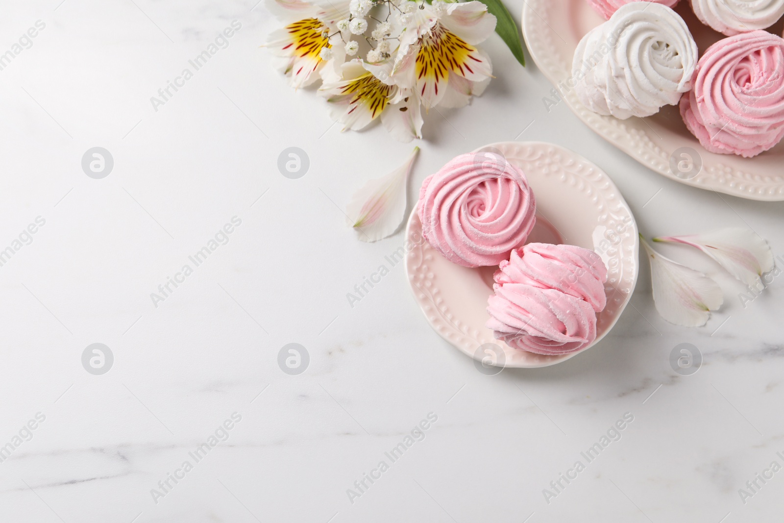 Photo of Different delicious zephyrs and flowers on white marble table, flat lay. Space for text