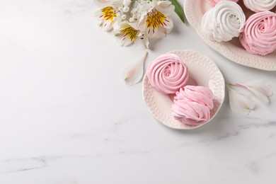 Photo of Different delicious zephyrs and flowers on white marble table, flat lay. Space for text