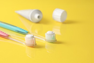 Photo of Brushes with toothpaste and tube on yellow background