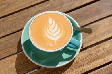 Cup of aromatic hot coffee and spoon on wooden table, above view